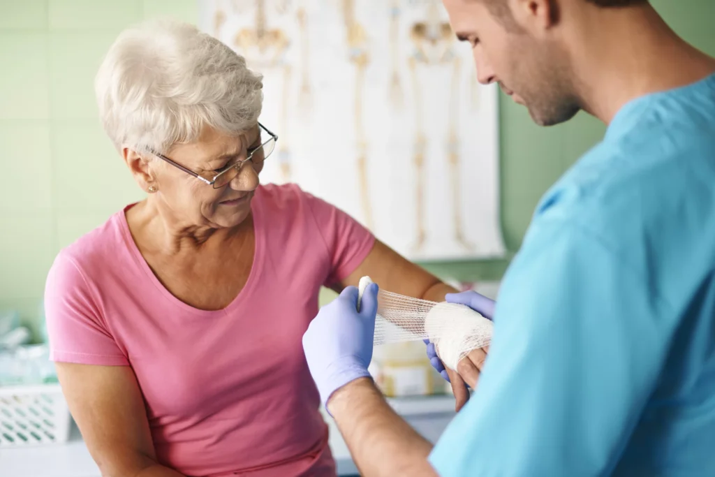 Doctor bandaging an elderly woman's arm during a wound care visit